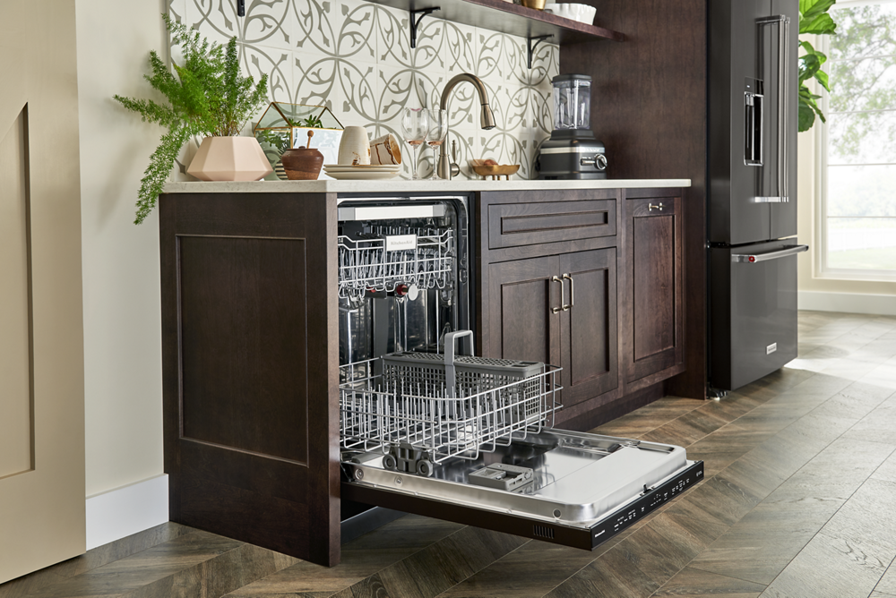 KitchenAid dishwasher with the door open in a kitchen full of dark cabinetry.